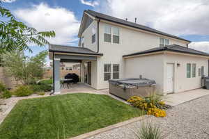 Back of property with stucco siding, a lawn, a hot tub, a fenced backyard, and a patio area