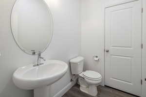 Bathroom featuring toilet, wood finished floors, baseboards, and a sink