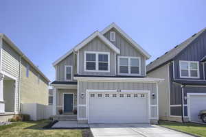 View of front of home with board and batten siding, fence, an attached garage, and driveway