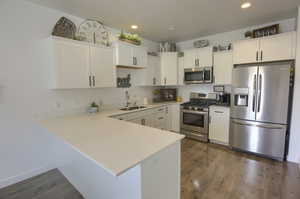 Kitchen with wood finished floors, a sink, light countertops, white cabinets, and stainless steel appliances