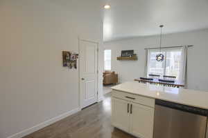 Kitchen featuring stainless steel dishwasher, dark wood-style floors, light countertops, white cabinets, and decorative light fixtures