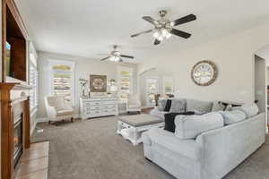 Carpeted living area with baseboards, arched walkways, a glass covered fireplace, and ceiling fan