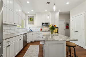 Kitchen featuring appliances with stainless steel finishes, a sink, a center island, white cabinetry, and tasteful backsplash