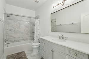 Bathroom featuring visible vents, vanity, marble finish floor, toilet, and shower / bath combo