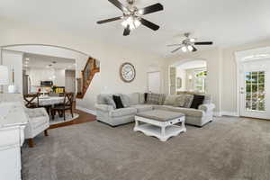 Living room featuring arched walkways, a ceiling fan, baseboards, and stairway