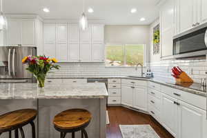 Kitchen with a sink, a kitchen breakfast bar, stainless steel appliances, and white cabinetry