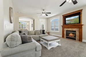 Living room with carpet flooring, baseboards, arched walkways, a tiled fireplace, and a ceiling fan
