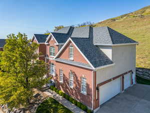 View of side of property with concrete driveway, brick siding, a shingled roof, and a garage
