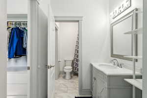 Bathroom with vanity, toilet, marble finish floor, baseboards, and a spacious closet