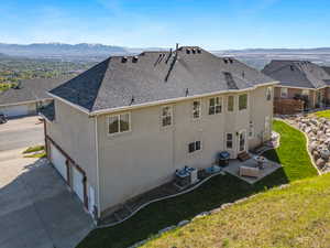 Back of house with a lawn, a shingled roof, a mountain view, and stucco siding