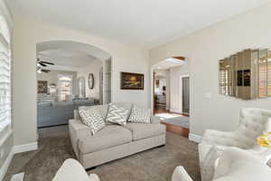 Carpeted living area featuring baseboards, arched walkways, ceiling fan, and visible vents