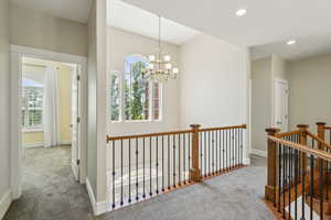 Hall with carpet floors, baseboards, a notable chandelier, and an upstairs landing