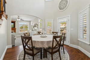 Dining room with a ceiling fan, baseboards, a high ceiling, a tiled fireplace, and arched walkways