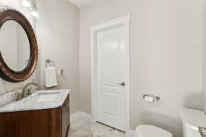 Half bathroom with baseboards, vanity, toilet, and marble finish floor