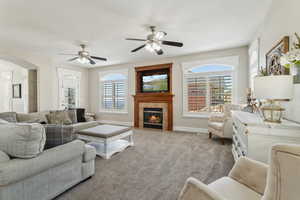 Carpeted living area featuring a tiled fireplace, arched walkways, baseboards, and a ceiling fan