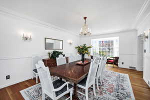 Dining room featuring wood finished floors, crown molding, visible vents, baseboards, and a chandelier