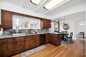 Kitchen featuring a sink, tasteful backsplash, beam ceiling, dishwasher, and light wood finished floors