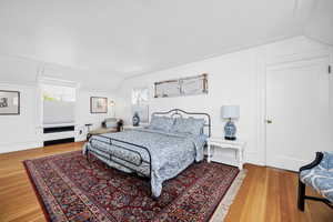 Bedroom with a decorative wall, wood finished floors, and lofted ceiling