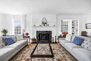 Living room with built in shelves, ornamental molding, a high end fireplace, and light wood-style floors