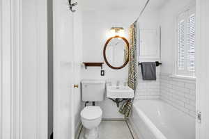 Bathroom featuring a tub, tile patterned floors, toilet, and a healthy amount of sunlight
