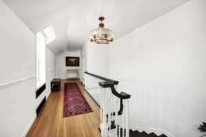 Hall featuring light wood-type flooring, a chandelier, and an upstairs landing