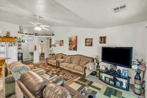 Living room featuring vaulted ceiling, visible vents, and ceiling fan