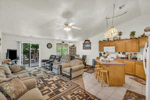 Living area with vaulted ceiling, light tile patterned flooring, a ceiling fan, and visible vents
