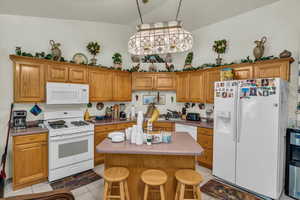 Kitchen with white appliances, brown cabinets, a kitchen bar, light tile patterned floors, and a kitchen island