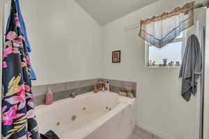Bathroom with tile patterned flooring, lofted ceiling, baseboards, and a jetted tub