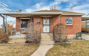 Bungalow featuring covered porch, a front lawn, a chimney, and brick siding