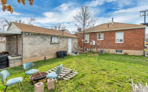 Rear view of house with an outdoor fire pit, a yard, and a shingled roof
