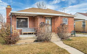 Bungalow-style home with a chimney, covered porch, and a front lawn