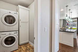 Clothes washing area featuring a sink, a textured ceiling, stacked washer / drying machine, and cabinet space