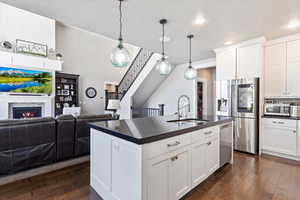 Kitchen featuring a sink, dark countertops, open floor plan, appliances with stainless steel finishes, and dark wood-style floors
