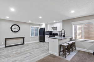 Kitchen with a sink, baseboards, black appliances, and white cabinets
