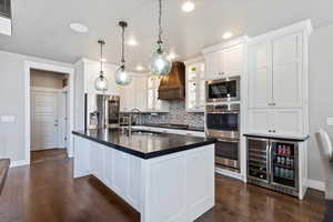 Kitchen featuring a sink, wine cooler, backsplash, dark countertops, and appliances with stainless steel finishes