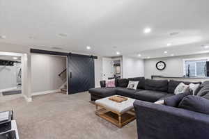 Living area with stairway, light colored carpet, a barn door, and recessed lighting