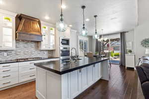 Kitchen featuring dark wood finished floors, dark countertops, appliances with stainless steel finishes, and custom exhaust hood