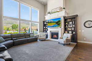Living area featuring plenty of natural light, dark wood-type flooring, a warm lit fireplace, and a towering ceiling