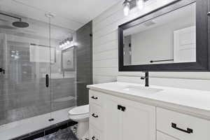 Full bathroom with a stall shower, a textured ceiling, toilet, visible vents, and vanity