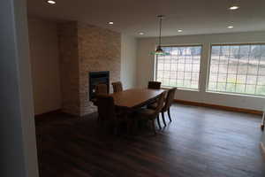 Dining area with baseboards, dark wood-style flooring, a stone fireplace, and recessed lighting