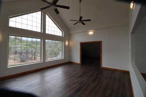 Unfurnished living room with baseboards, ceiling fan, high vaulted ceiling, and dark wood-type flooring