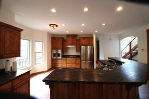 Kitchen with under cabinet range hood, dark countertops, appliances with stainless steel finishes, and a sink