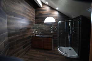 Bathroom featuring a stall shower, tile walls, vaulted ceiling, vanity, and wood finished floors