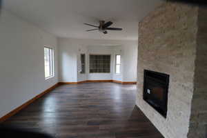 Unfurnished living room featuring a stone fireplace, baseboards, a ceiling fan, and wood finished floors