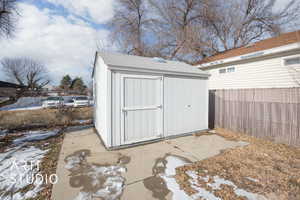 Snow covered structure featuring an outbuilding, a shed, and a fenced backyard