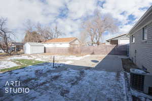 Snowy yard with an outdoor structure, a storage shed, central AC, a residential view, and a fenced backyard