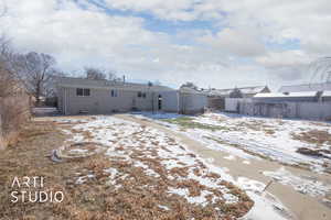 Snow covered back of property featuring fence, brick siding, and an outdoor structure