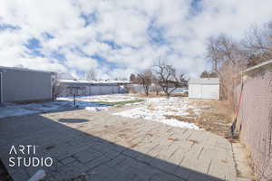 Yard layered in snow with a storage shed, an outbuilding, fence, and a patio
