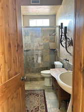Bathroom featuring a stall shower, stone tile floors, toilet, visible vents, and vanity